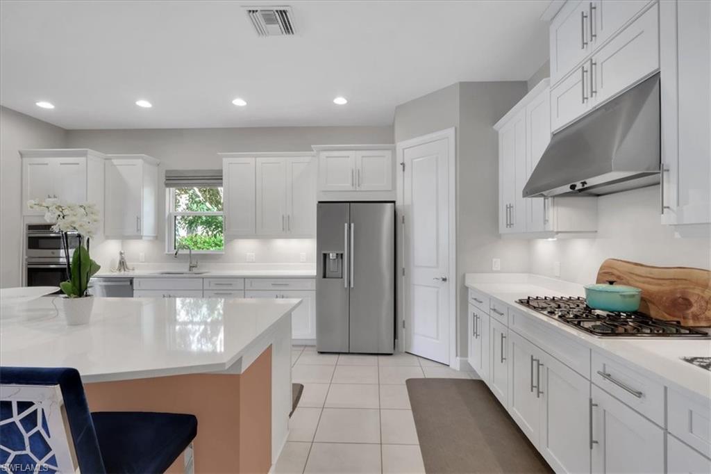 Kitchen with appliances with stainless steel finishes, under cabinet range hood, white cabinetry, light stone countertops, and a breakfast bar area