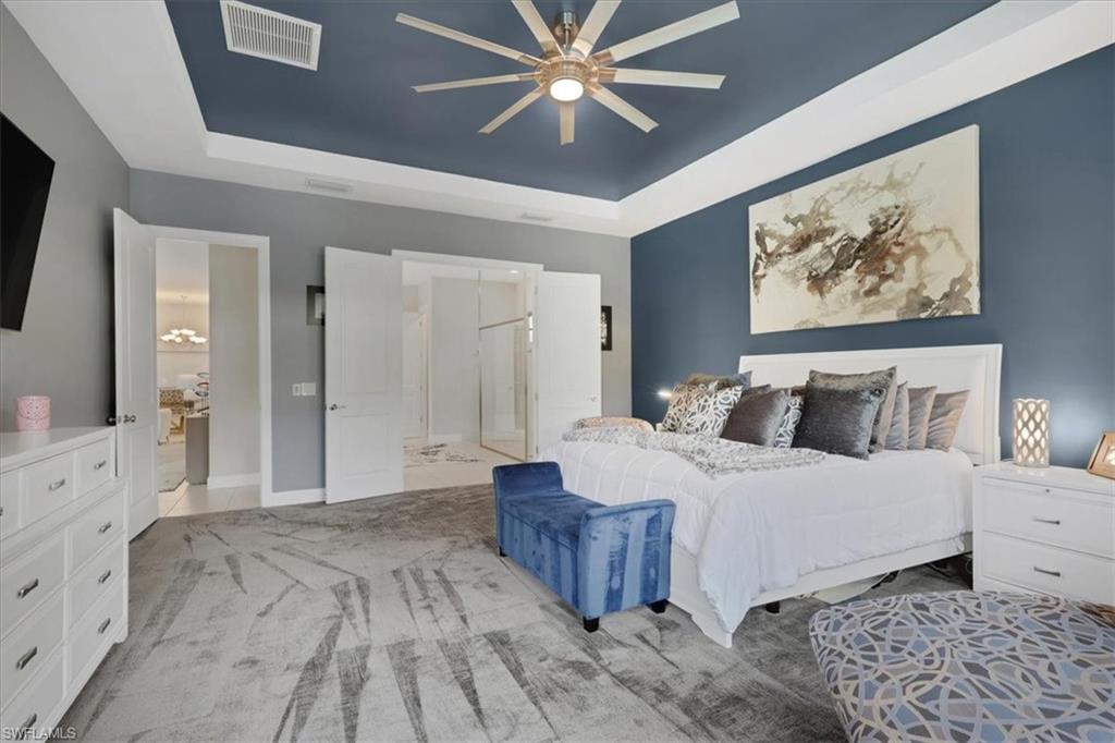 Carpeted bedroom with a tray ceiling, a ceiling fan, and connected bathroom