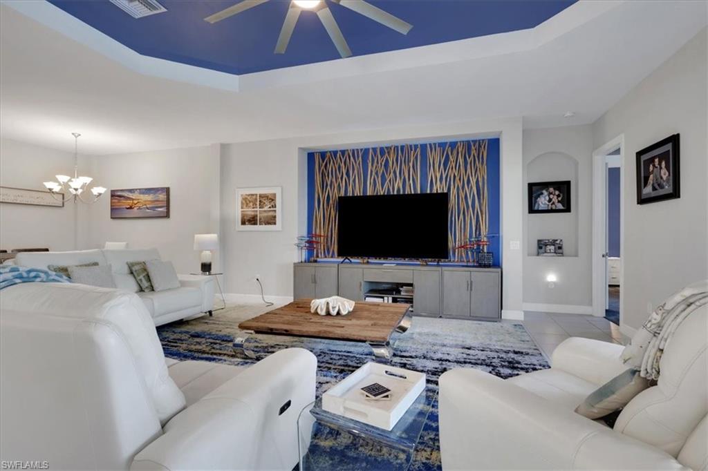 Tiled living room featuring a raised ceiling, a chandelier, and ceiling fan