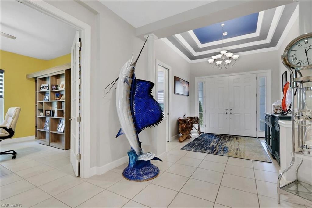 Entrance foyer with a raised ceiling, a chandelier, crown molding, and light tile patterned floors