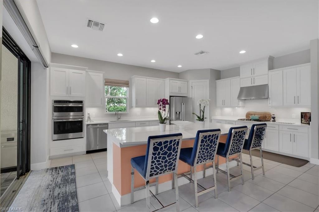 Kitchen with a breakfast bar area, stainless steel appliances, a center island, white cabinetry, and under cabinet range hood