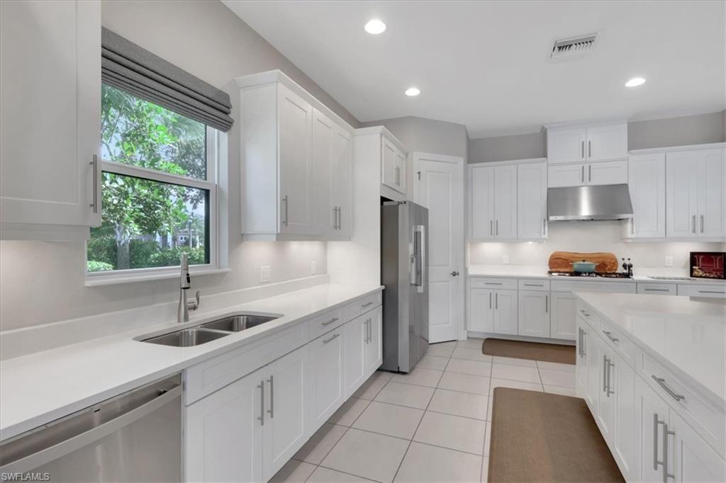 Kitchen with stainless steel appliances, white cabinets, under cabinet range hood, light stone countertops, and recessed lighting