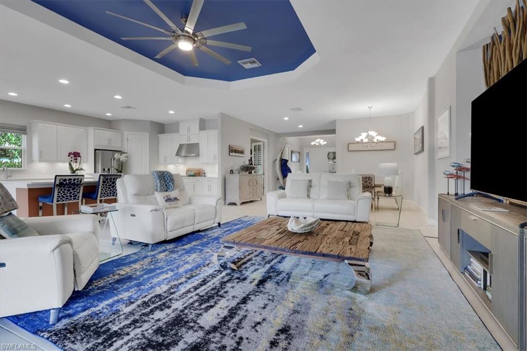 Living room featuring a ceiling fan, recessed lighting, a chandelier, and a tray ceiling