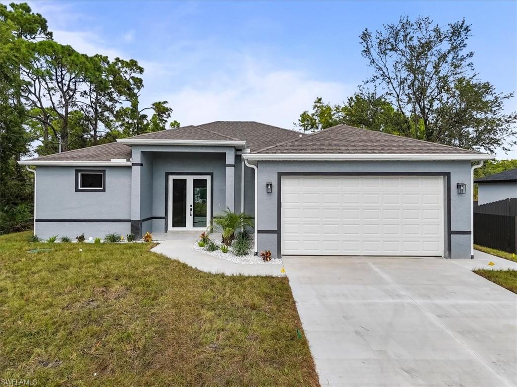 View of front of property featuring concrete driveway, a front yard, roof with shingles, an attached garage, and stucco siding