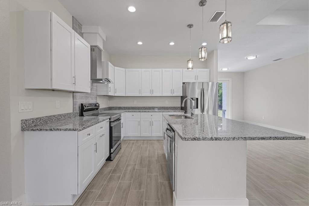 Kitchen featuring appliances with stainless steel finishes, decorative light fixtures, white cabinets, light stone counters, and recessed lighting