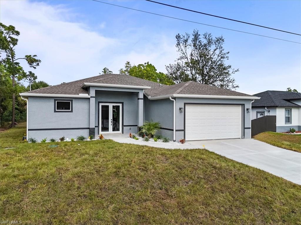 View of front facade with a front yard, stucco siding, concrete driveway, an attached garage, and french doors