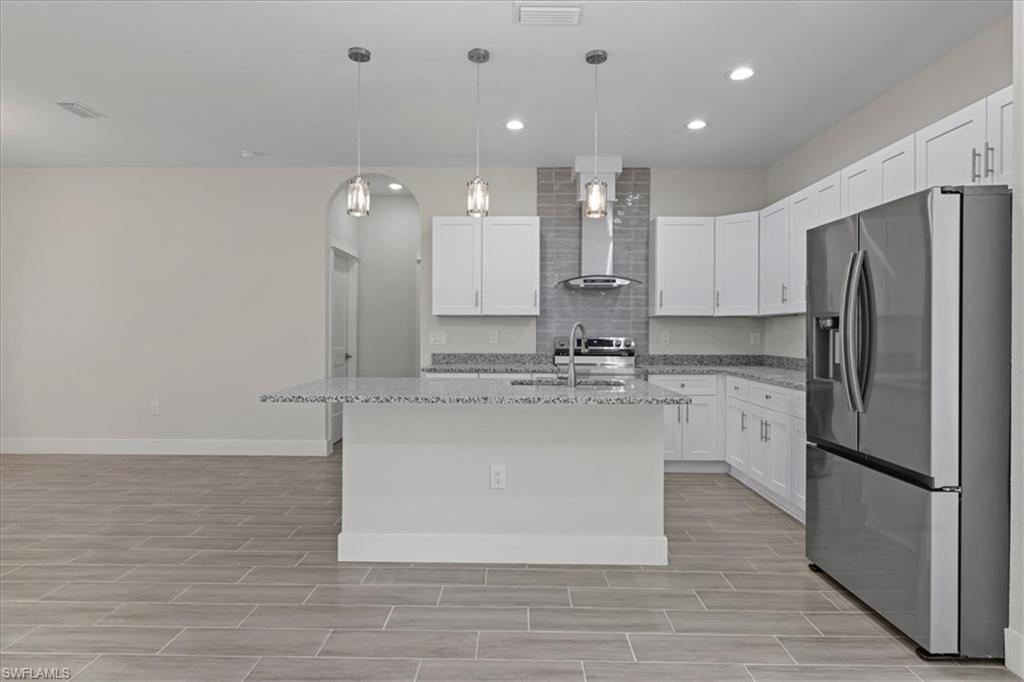 Kitchen featuring appliances with stainless steel finishes, light stone countertops, white cabinetry, hanging light fixtures, and recessed lighting