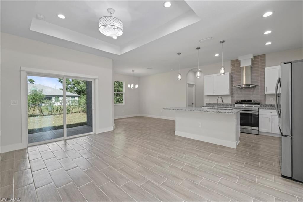 Kitchen featuring a chandelier, stainless steel appliances, a center island with sink, light stone countertops, and recessed lighting