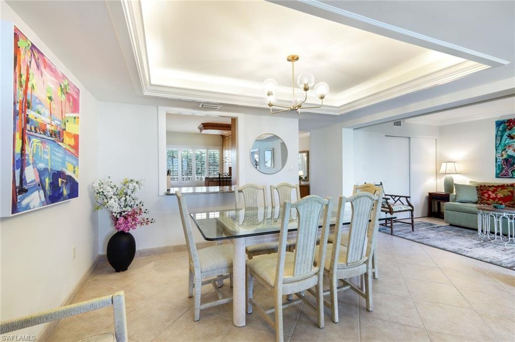 Tiled dining room featuring a chandelier, crown molding, and a raised ceiling