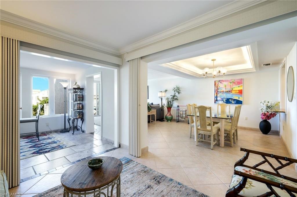 Dining area with a raised ceiling, light tile patterned floors, crown molding, and a chandelier