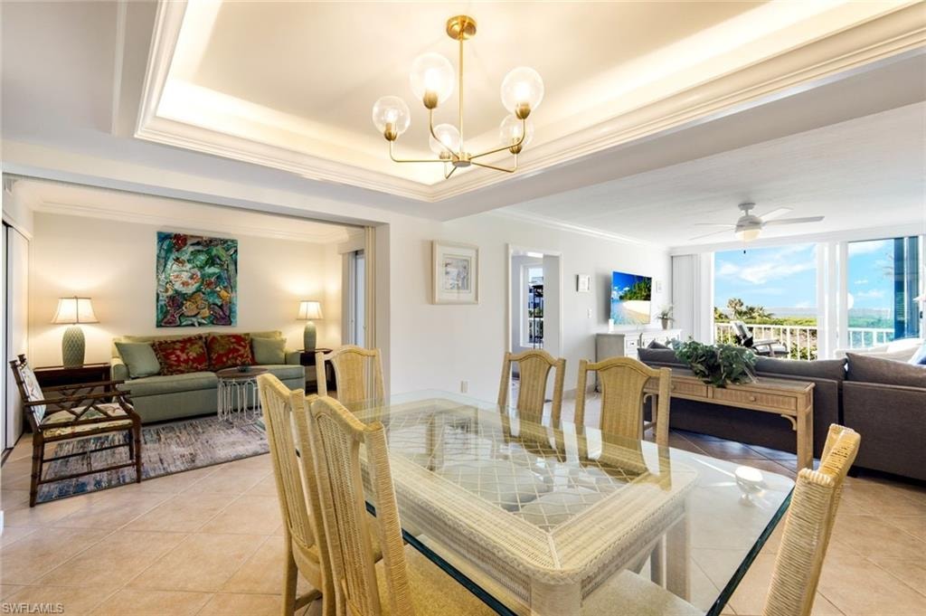 Dining area featuring light tile patterned flooring, crown molding, ceiling fan, a chandelier, and a raised ceiling