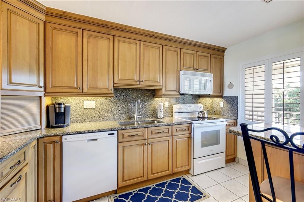 Kitchen featuring white appliances, brown cabinets, light tile patterned floors, tasteful backsplash, and light stone countertops