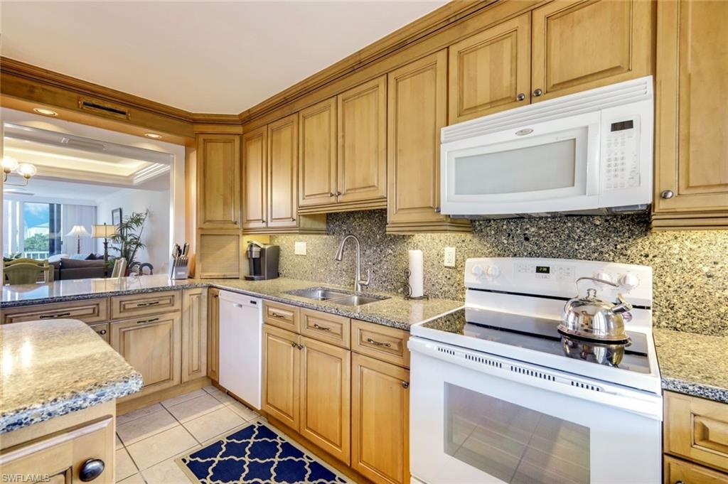 Kitchen with white appliances, light stone countertops, light tile patterned floors, decorative backsplash, and a tray ceiling