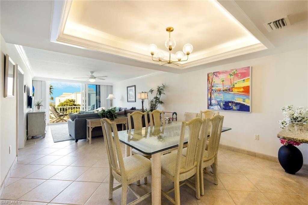 Dining space with a chandelier, light tile patterned floors, a ceiling fan, crown molding, and a tray ceiling