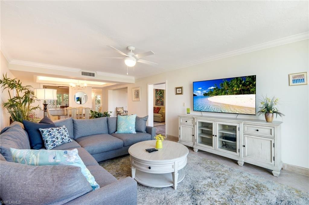 Tiled living area featuring ornamental molding, ceiling fan, and a chandelier