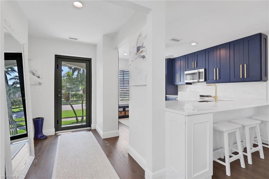 Kitchen featuring blue cabinets, backsplash, a kitchen breakfast bar, light stone countertops, and stainless steel microwave