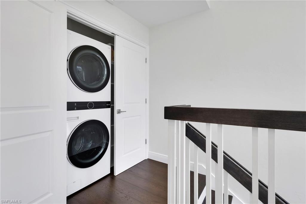 Washroom with stacked washing machine and dryer and dark wood finished floors