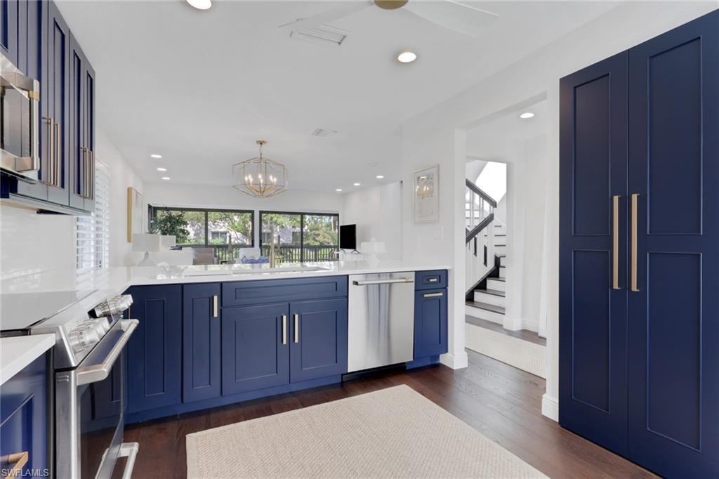 Kitchen with blue cabinets, appliances with stainless steel finishes, light stone countertops, dark wood finished floors, and hanging light fixtures