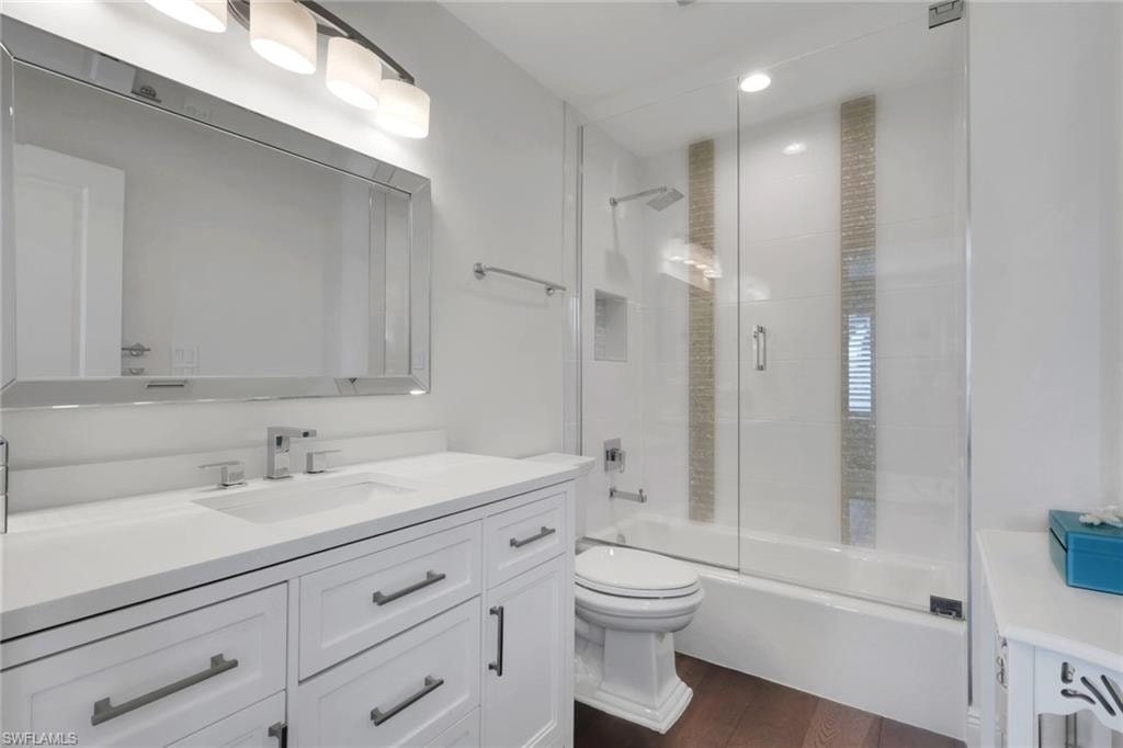Full bathroom with vanity, bath / shower combo with glass door, and dark wood-style floors