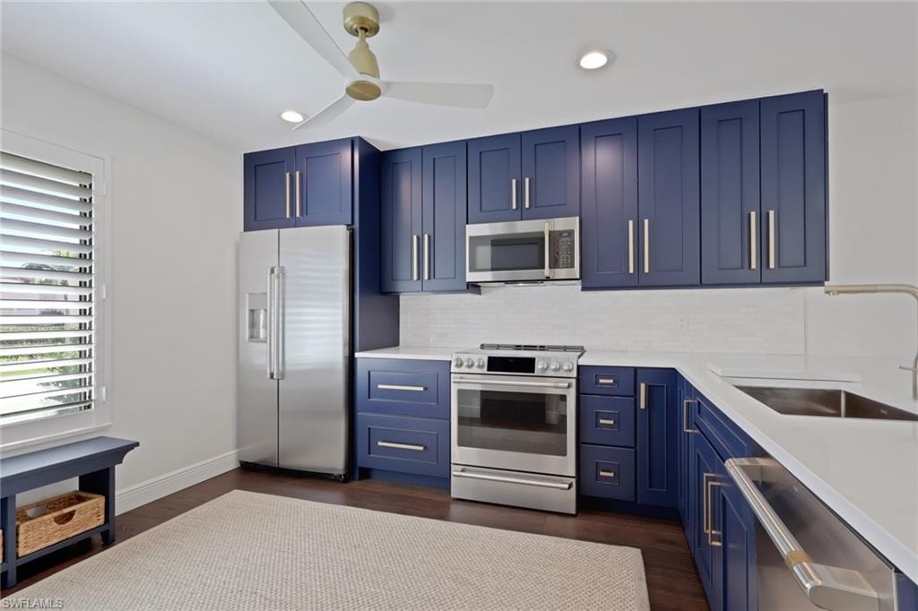Kitchen with blue cabinetry, stainless steel appliances, light stone counters, dark wood-style floors, and recessed lighting