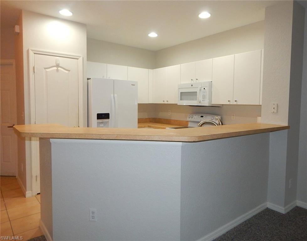 Kitchen with white appliances, light countertops, a peninsula, white cabinetry, and recessed lighting
