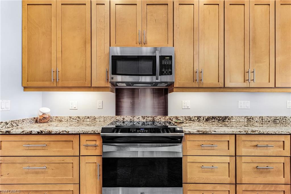 Kitchen featuring slide in range oven, stainless steel microwave, and light stone counters