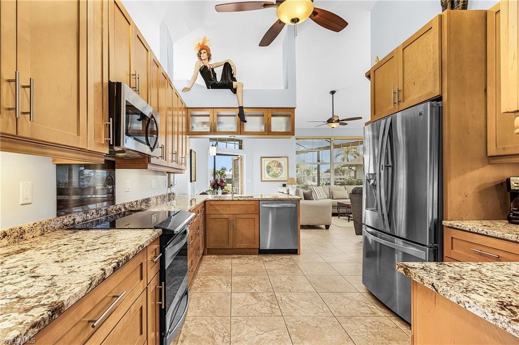 Kitchen with stainless steel appliances, light stone counters, brown cabinets, a ceiling fan, and open floor plan