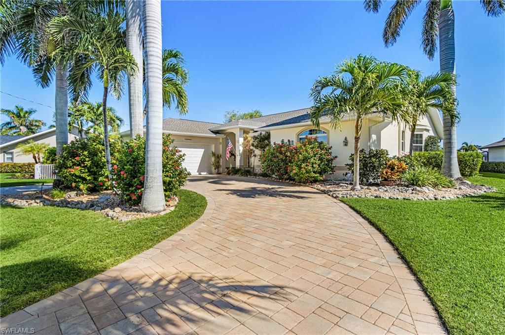 Ranch-style home with a front yard, stucco siding, an attached garage, and decorative driveway