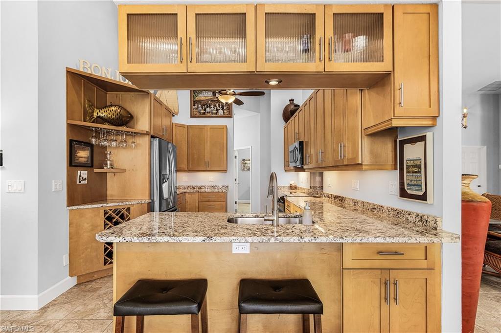 Kitchen with light stone countertops, glass insert cabinets, a breakfast bar area, and a peninsula