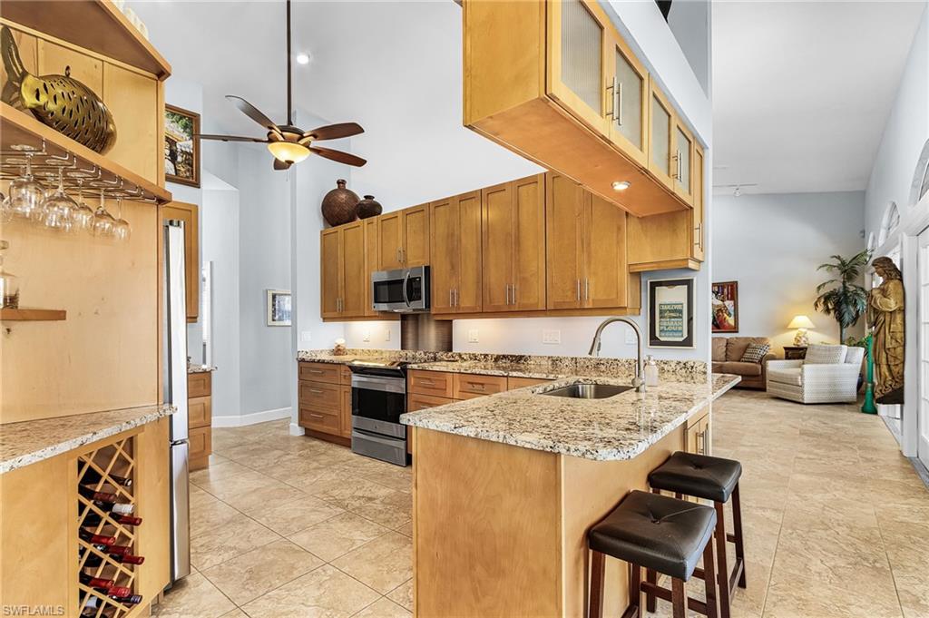 Kitchen with a high ceiling, a peninsula, stainless steel appliances, a kitchen breakfast bar, and glass insert cabinets