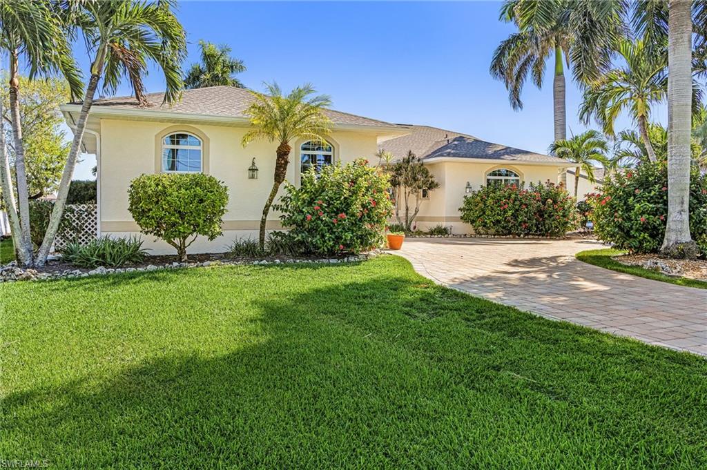 View of front facade with stucco siding, a front yard, decorative driveway, and a shingled roof
