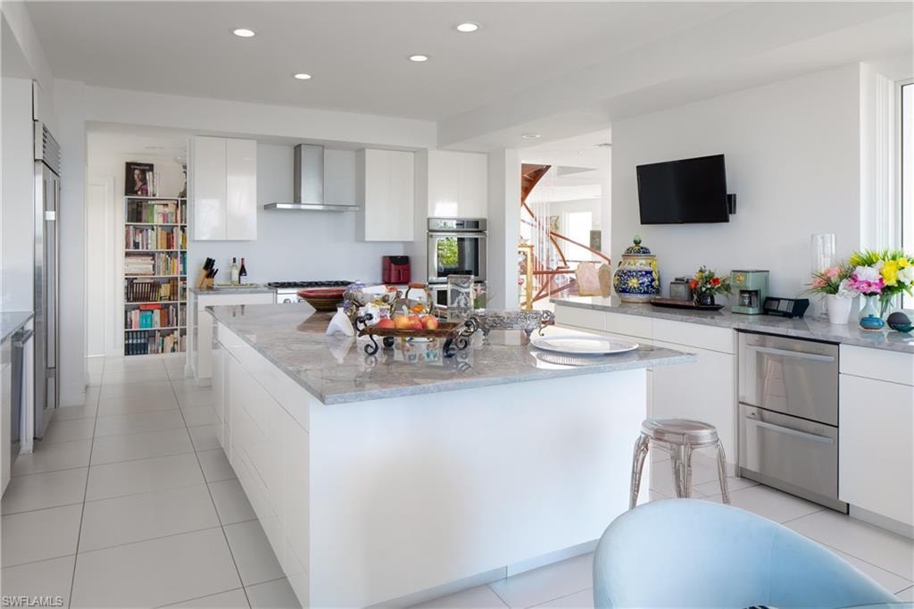 Kitchen with white cabinetry, light stone countertops, wall chimney exhaust hood, light tile patterned floors, and recessed lighting