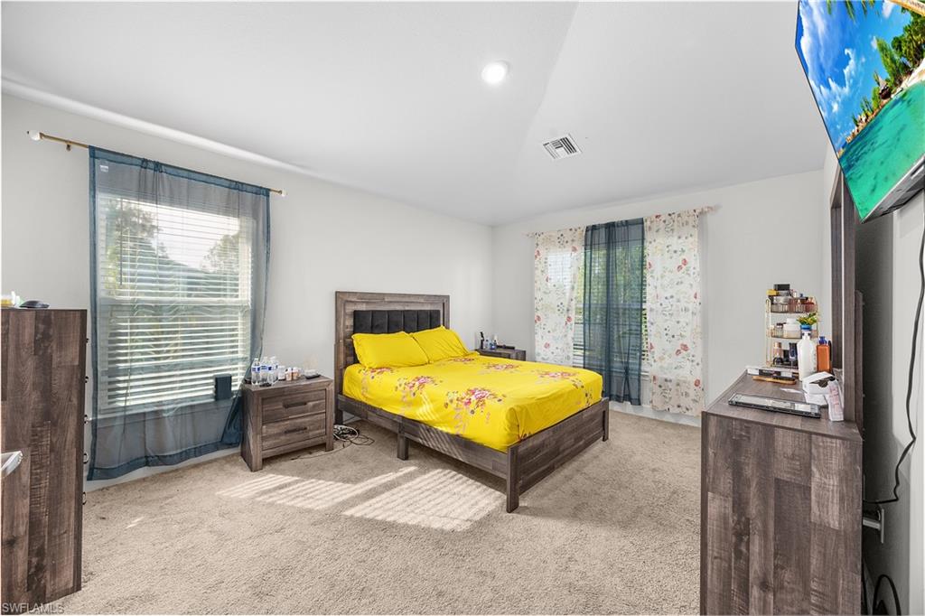 Bedroom with light carpet, lofted ceiling, and multiple windows