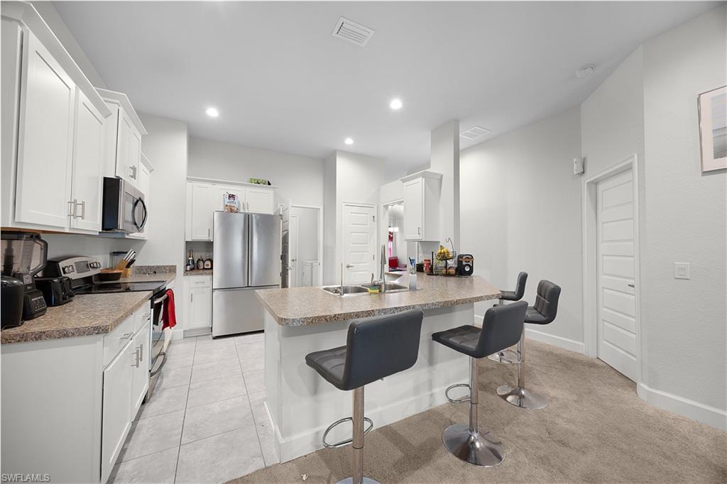 Kitchen featuring a kitchen bar, appliances with stainless steel finishes, a peninsula, white cabinets, and light tile patterned floors