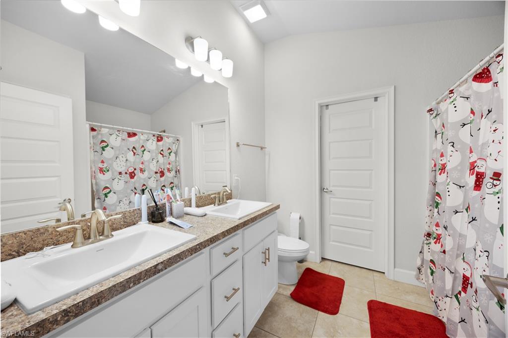 Bathroom featuring double vanity, light tile patterned floors, a shower with curtain, and vaulted ceiling