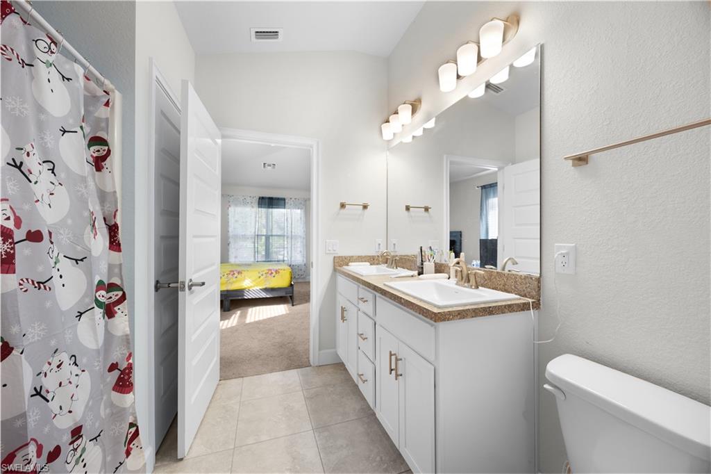 Ensuite bathroom with double vanity, light tile patterned floors, curtained shower, light colored carpet, and a textured wall