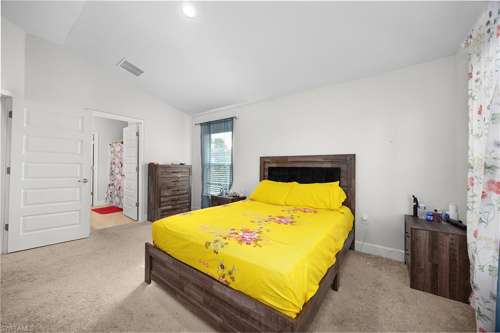 Bedroom with light carpet, vaulted ceiling, and ensuite bathroom