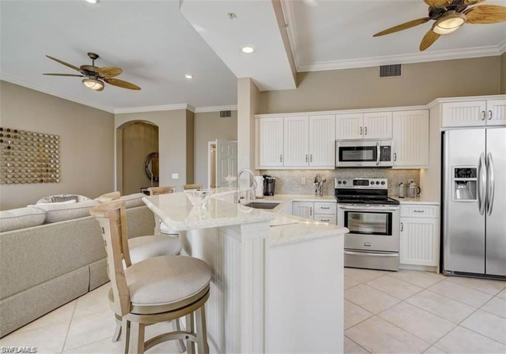 Kitchen featuring ceiling fan, a kitchen breakfast bar, crown molding, appliances with stainless steel finishes, and light tile patterned floors
