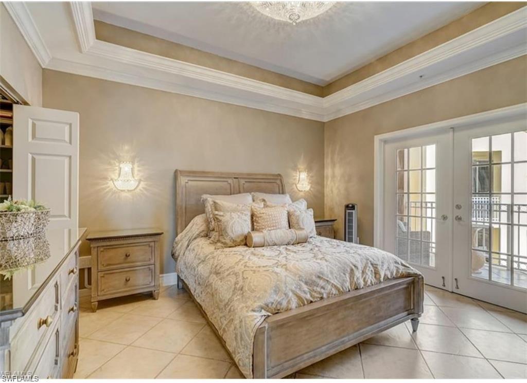 Bedroom with french doors, a tray ceiling, access to exterior, light tile patterned flooring, and ornamental molding