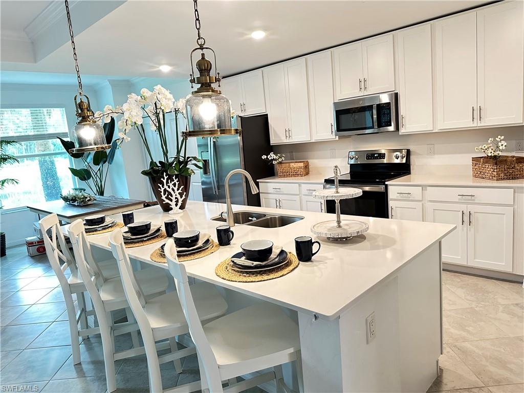 Kitchen with sink, appliances with stainless steel finishes, white cabinets, and an island with sink