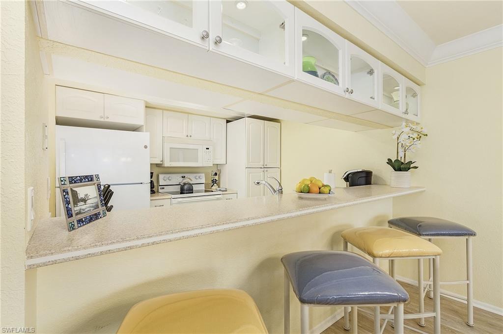 Kitchen with crown molding, a breakfast bar, light wood-type flooring, white cabinetry, and white appliances