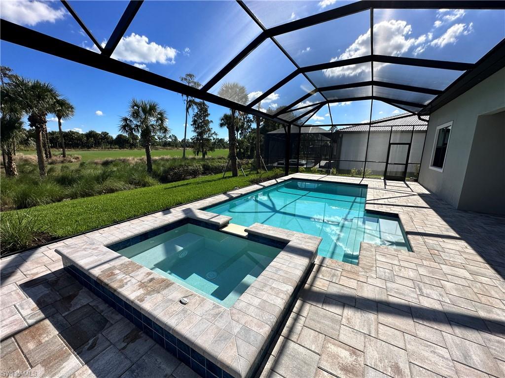 View of swimming pool with a patio area, a pool with connected hot tub, a sunroom, glass enclosure, and a lawn