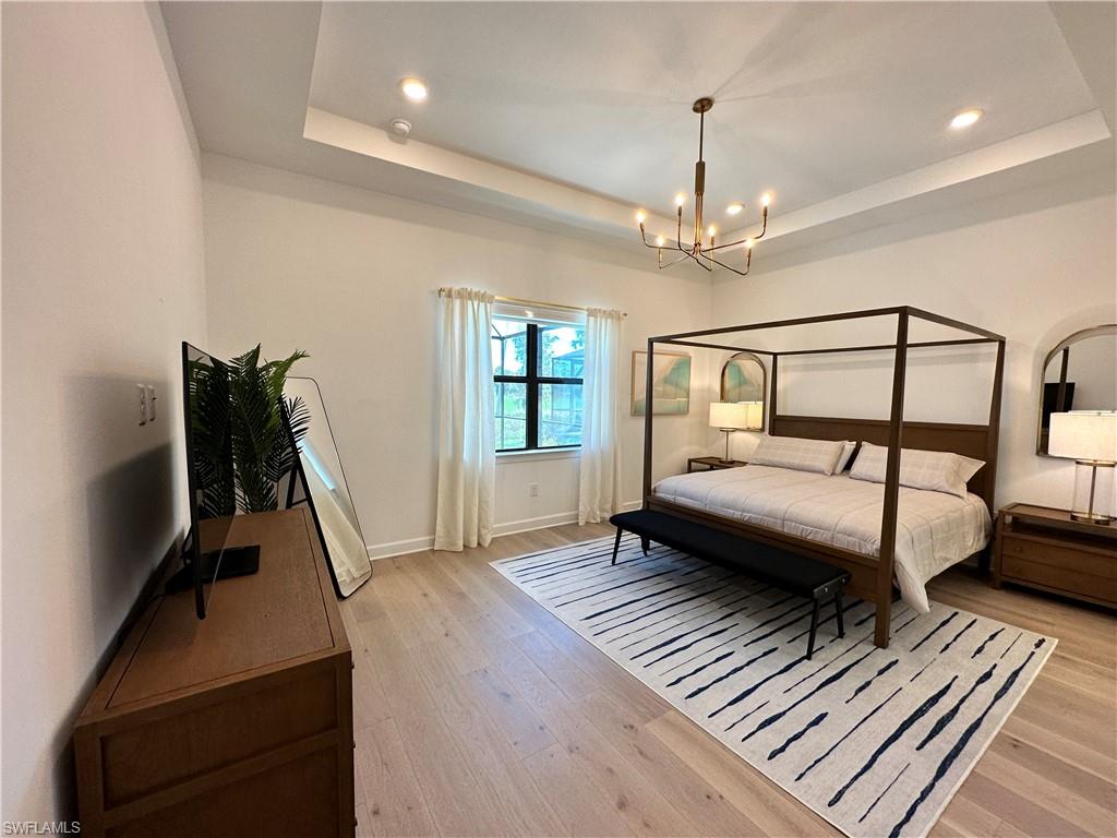 Bedroom featuring a raised ceiling, a chandelier, light wood finished floors, and recessed lighting