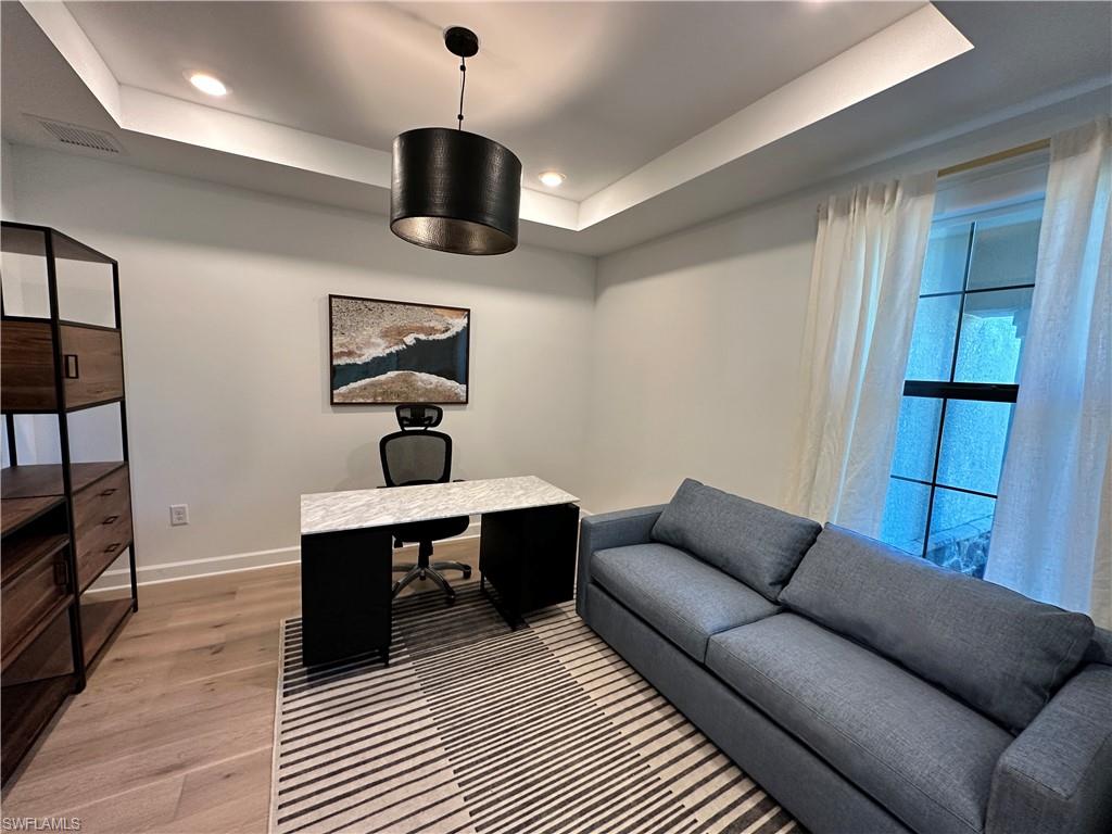 Home office with light wood-style flooring, a tray ceiling, and recessed lighting