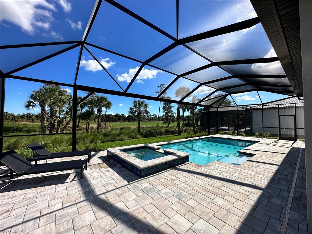 View of swimming pool featuring a sunroom, a pool with connected hot tub, glass enclosure, and a patio