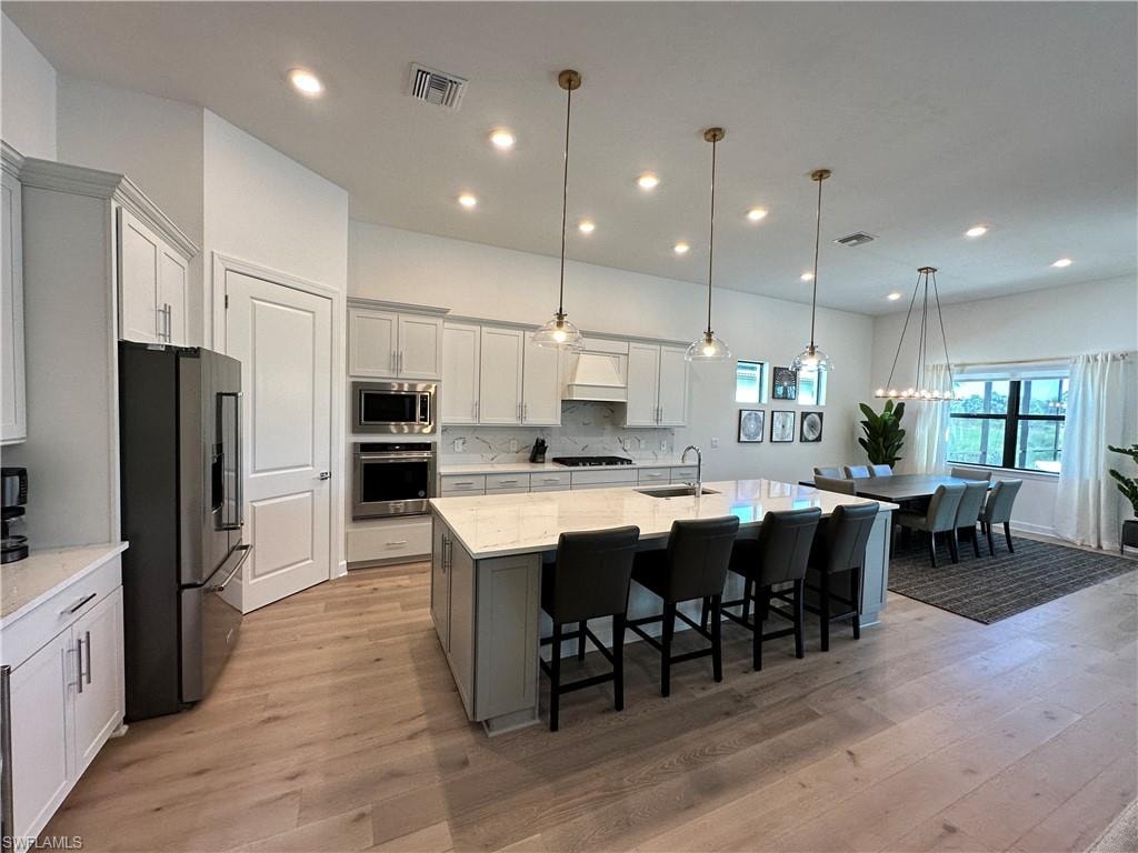 Kitchen with hanging light fixtures, a kitchen breakfast bar, a kitchen island with sink, stainless steel appliances, and gray cabinetry