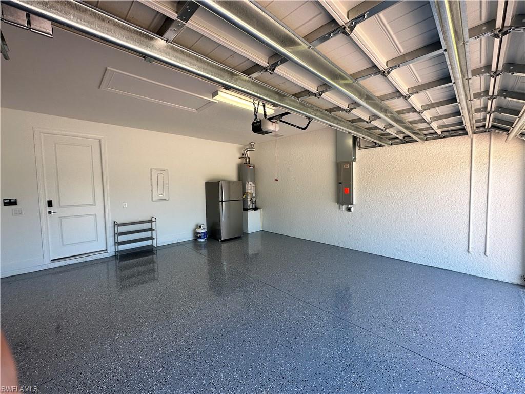 Garage with freestanding refrigerator, electric panel, and water heater