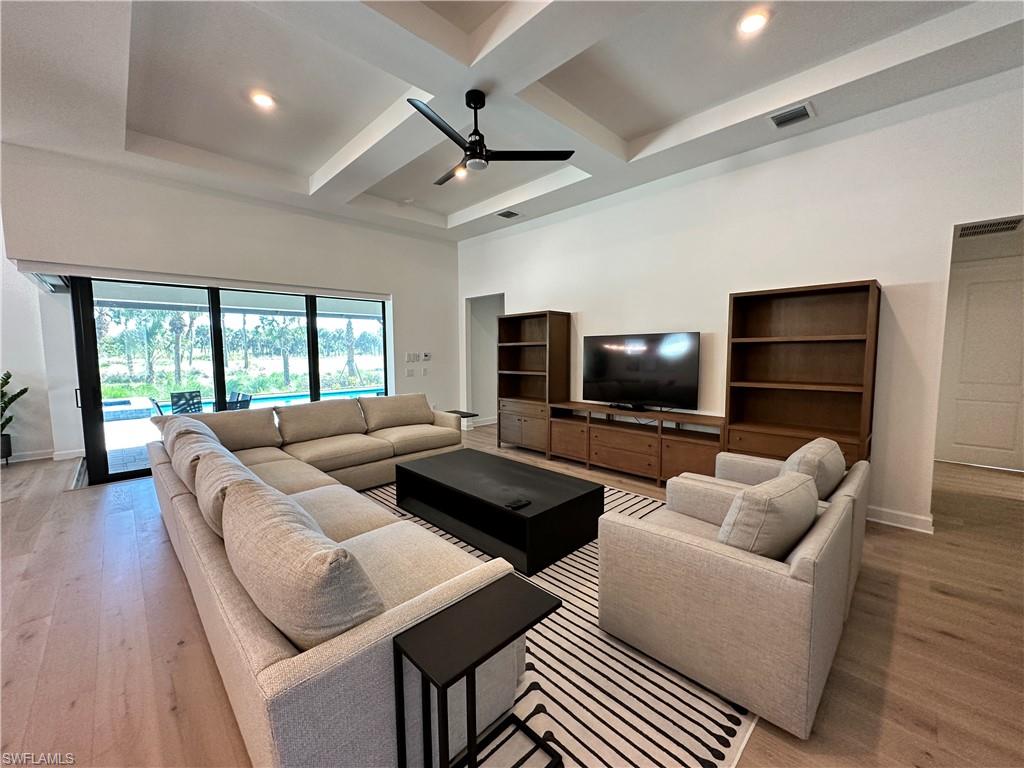 Living room featuring coffered ceiling, light wood finished floors, beam ceiling, a ceiling fan, and a high ceiling