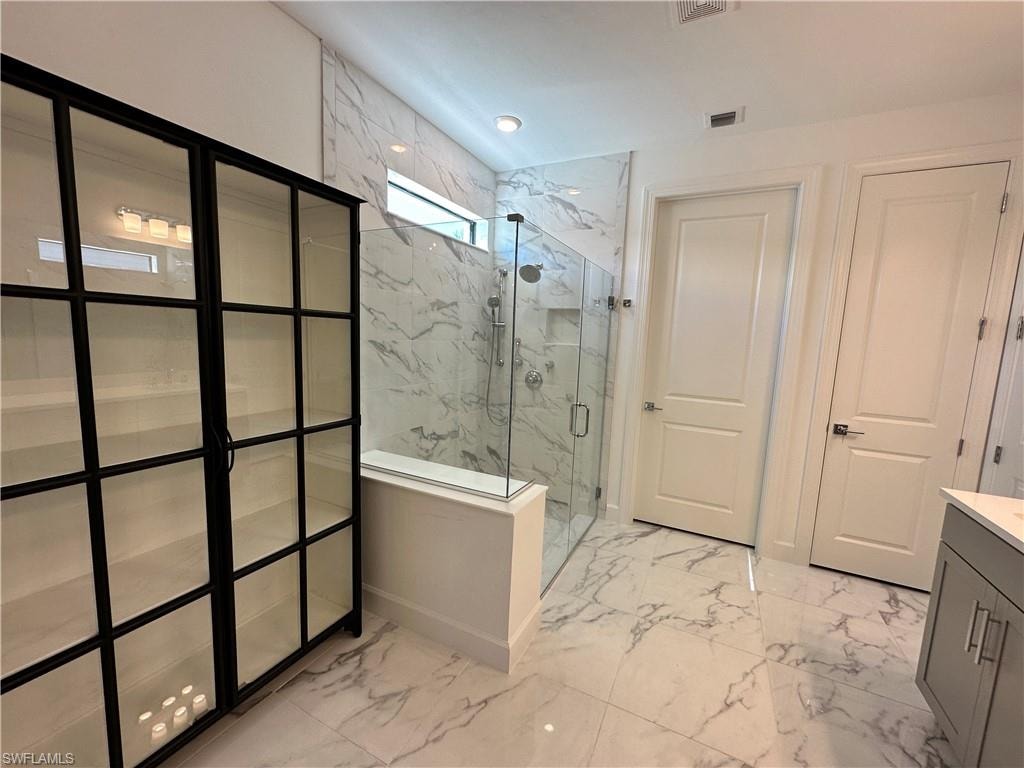 Full bath featuring light marble finish floors, a marble finish shower, and vanity