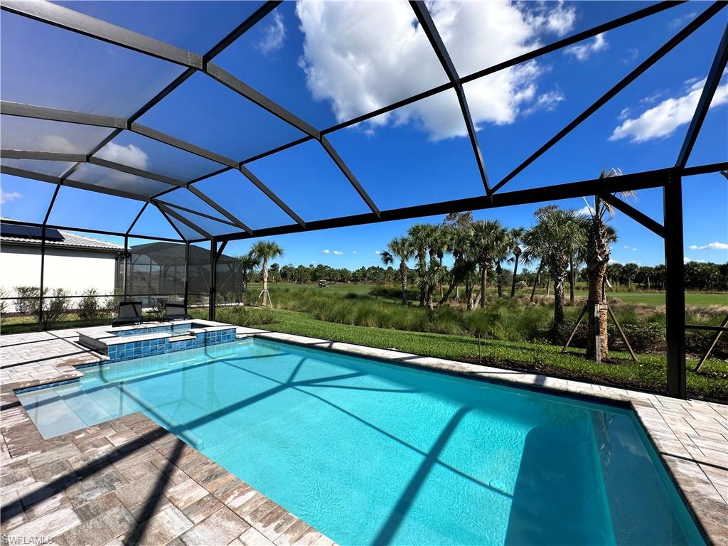 View of swimming pool featuring glass enclosure, a sunroom, a pool with connected hot tub, and a patio area